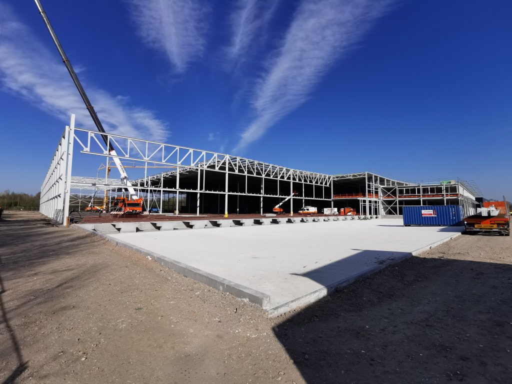 Bouwplaats met staalconstructies en kranen onder blauwe lucht.
